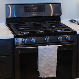 Black stainless steel propane kitchen range with a white and grey towel hanging from the front
